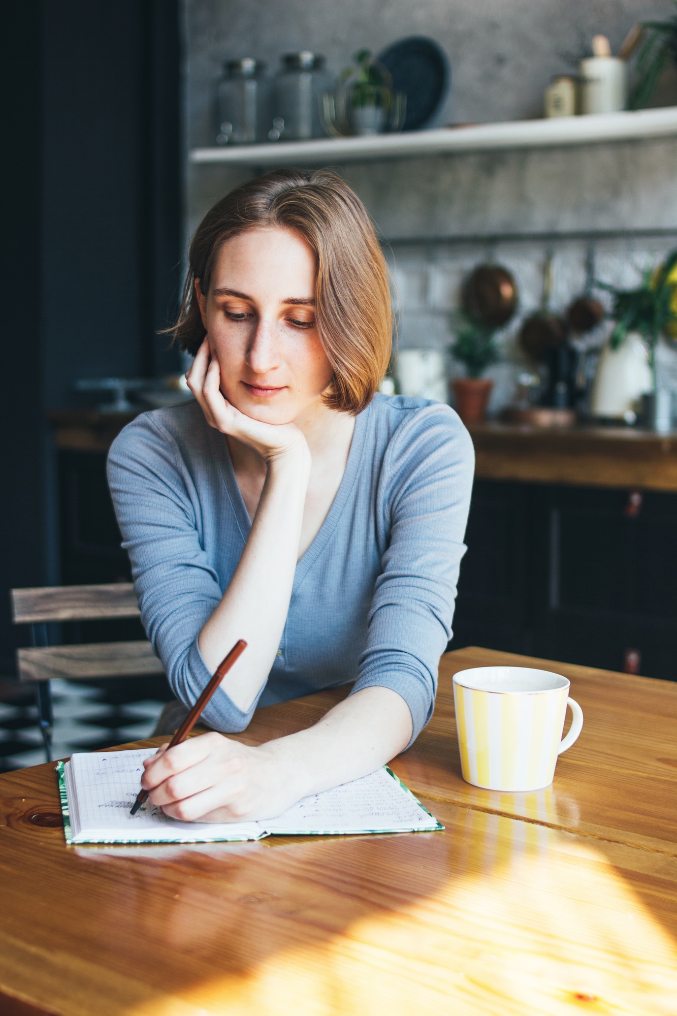Young woman southpaw lefthender calculates family budget, writes in diary in kitchen