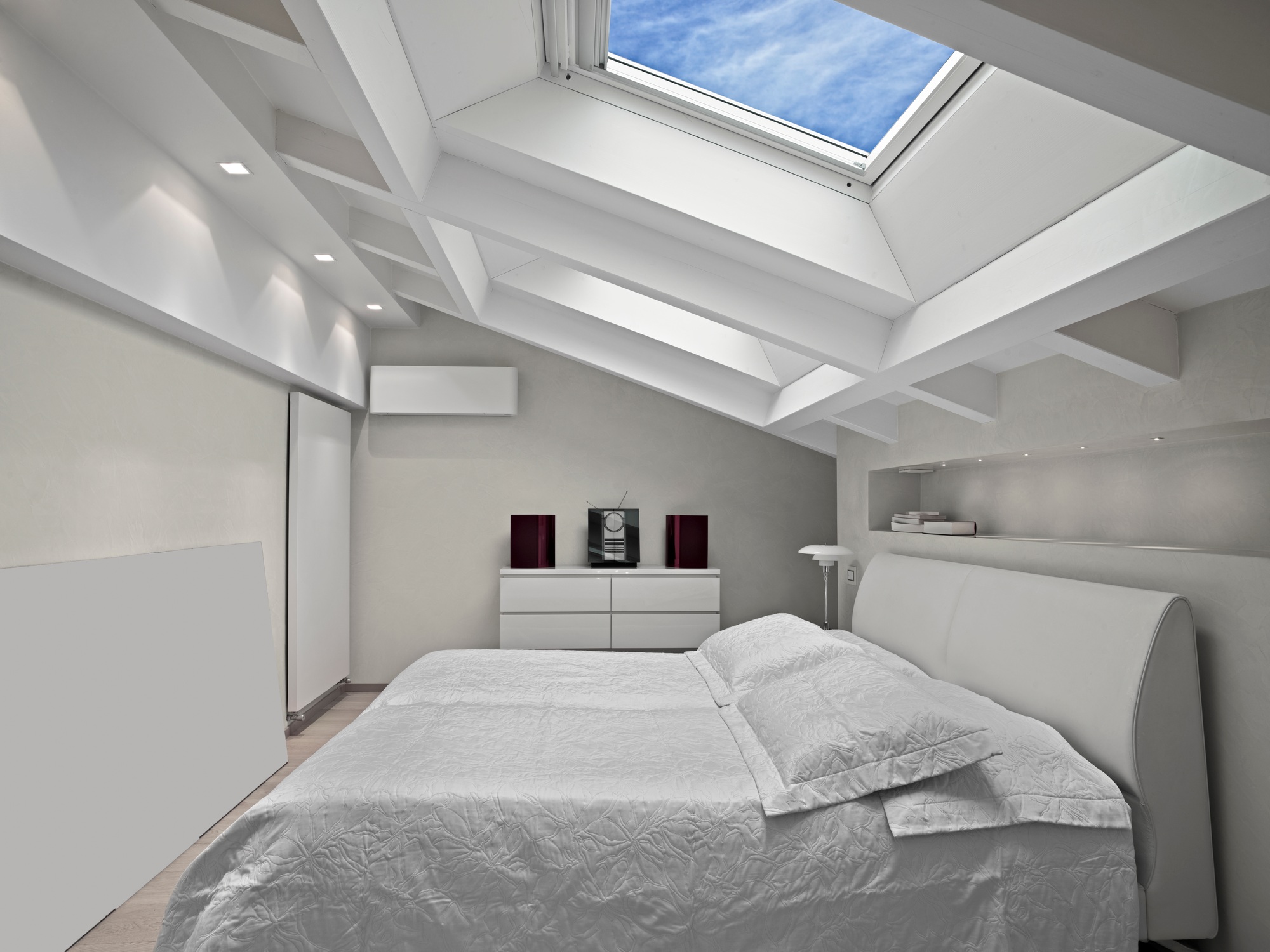 Bright modern attic bedroom with a large skylight, minimalist furnishings, neutral tones, and clean lines creating an airy and cozy luxury space